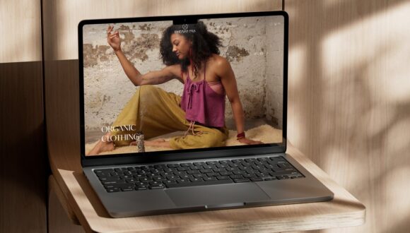 A laptop of a wooden shelf dappled by sunlight with the Bohemian Folk website on screen