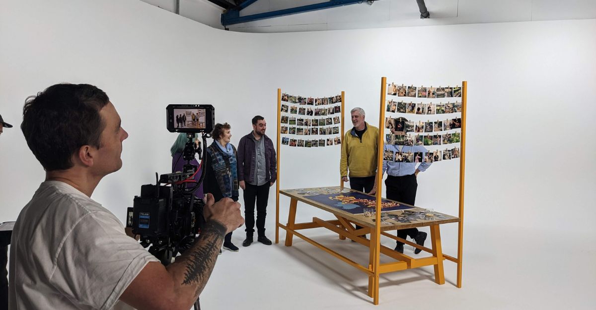Film studio. Man behind camera and actors on a set with a large table